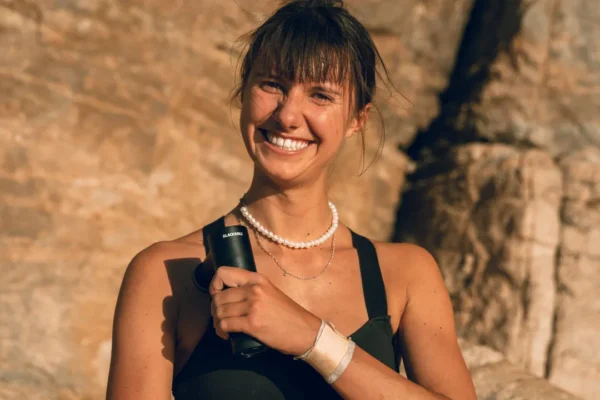 Femme souriante tenant un pistolet de massage type Theragun ou Hypervolt dans un cadre ensoleillé